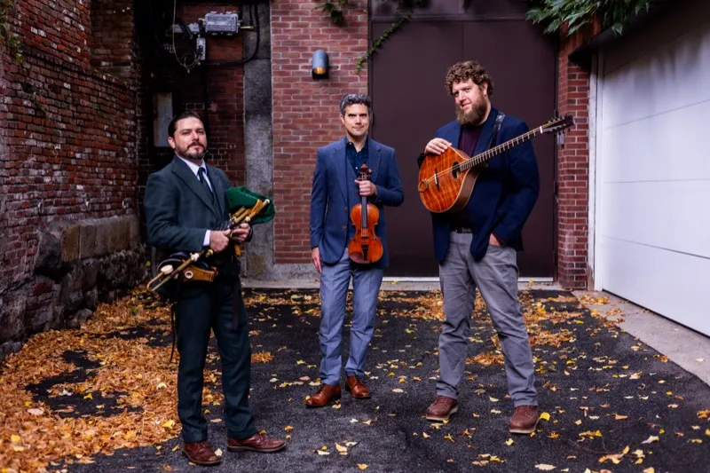 Joey Abarta, Nathan Gourley, and Owen Marshall standing with instruments in a brick alley